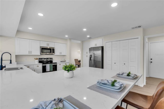 kitchen with kitchen peninsula, appliances with stainless steel finishes, sink, white cabinetry, and a breakfast bar area