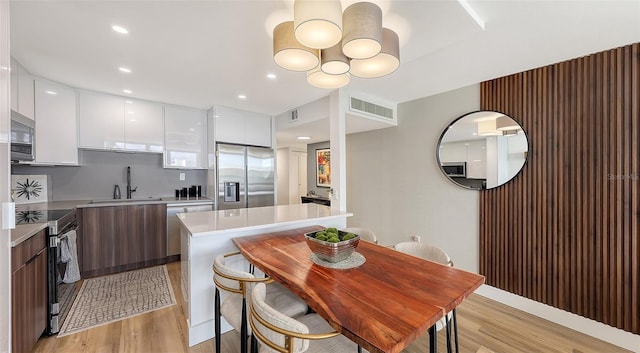 kitchen featuring white cabinetry, stainless steel appliances, sink, light wood-type flooring, and a center island