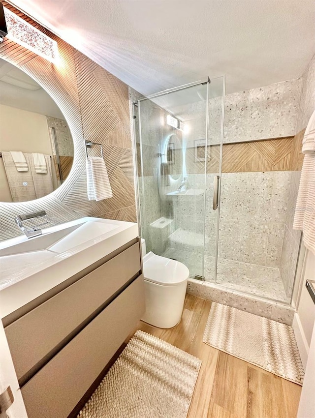 bathroom with a textured ceiling, wood-type flooring, a shower with door, vanity, and toilet