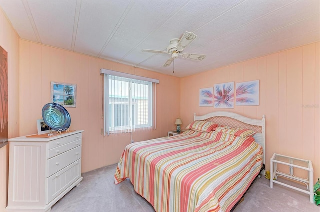 bedroom with ceiling fan, wood walls, and light colored carpet