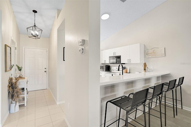 kitchen with white cabinetry, vaulted ceiling, decorative light fixtures, a kitchen bar, and stainless steel range with electric stovetop