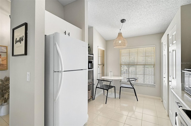 kitchen featuring white fridge, white cabinetry, hanging light fixtures, and light tile patterned floors