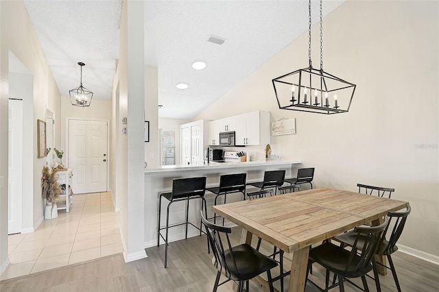 dining area with a textured ceiling, light hardwood / wood-style floors, and lofted ceiling