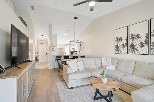 living room featuring ceiling fan with notable chandelier, light hardwood / wood-style flooring, and vaulted ceiling