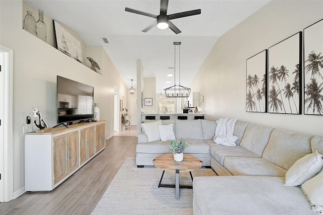 living room with ceiling fan with notable chandelier, sink, vaulted ceiling, a textured ceiling, and light hardwood / wood-style floors