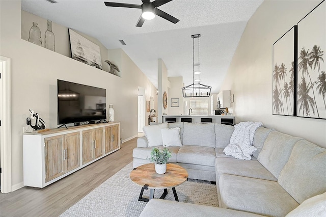 living room featuring light wood-type flooring, ceiling fan with notable chandelier, a textured ceiling, sink, and high vaulted ceiling