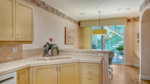 kitchen with kitchen peninsula, light wood-type flooring, tile countertops, and white dishwasher