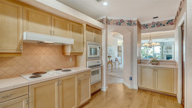 kitchen featuring tile countertops, light wood-type flooring, white appliances, and an inviting chandelier