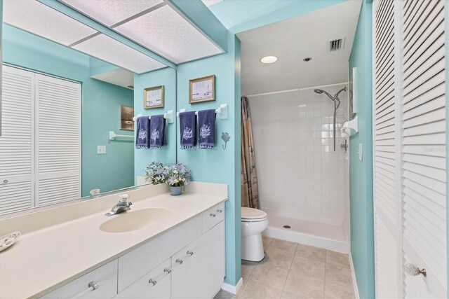 bathroom with toilet, a tile shower, vanity, and tile patterned floors