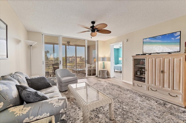living room with a wall of windows, light wood finished floors, ceiling fan, and a textured ceiling