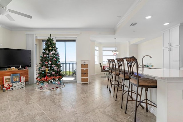 interior space with sink, a kitchen breakfast bar, pendant lighting, white cabinets, and ornamental molding