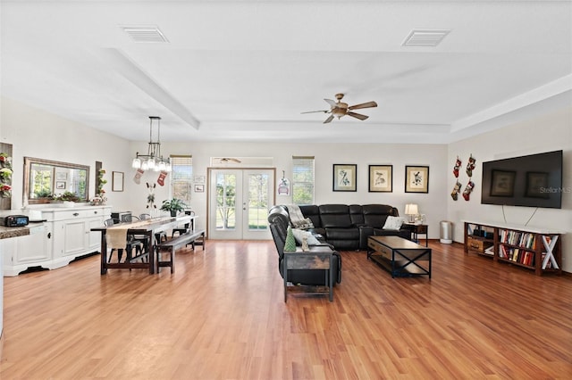 living room with a tray ceiling, ceiling fan, french doors, and light wood-type flooring