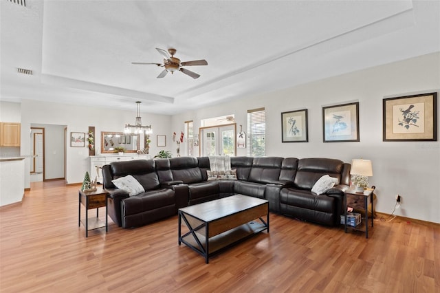 living room featuring ceiling fan with notable chandelier, light hardwood / wood-style floors, and a tray ceiling