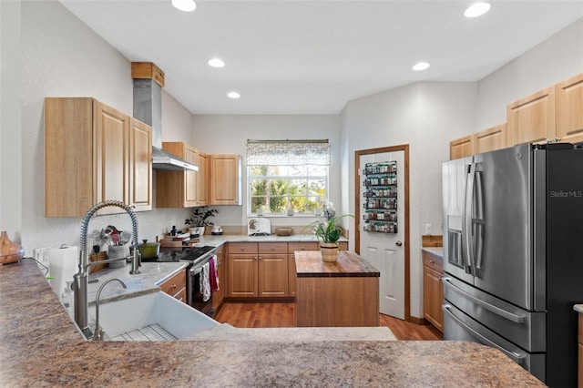 kitchen with stainless steel appliances, wall chimney range hood, light hardwood / wood-style flooring, light brown cabinetry, and a kitchen island