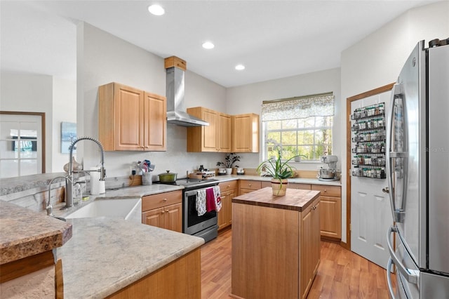 kitchen with a center island, light brown cabinets, stainless steel appliances, wall chimney range hood, and light hardwood / wood-style floors