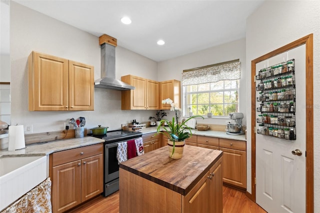 kitchen featuring stainless steel electric stove, wall chimney exhaust hood, a center island, and light hardwood / wood-style flooring