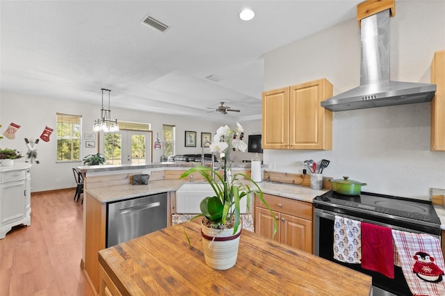 kitchen featuring appliances with stainless steel finishes, french doors, wall chimney exhaust hood, light hardwood / wood-style flooring, and hanging light fixtures