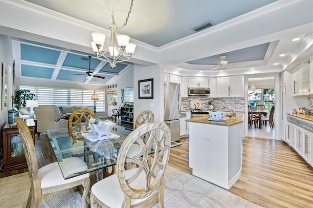 dining space featuring ceiling fan with notable chandelier, light hardwood / wood-style floors, ornamental molding, and coffered ceiling