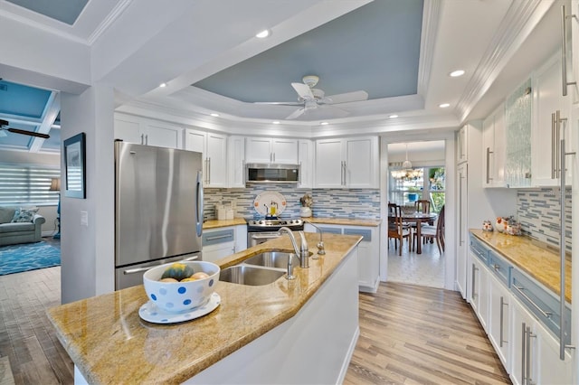 kitchen with white cabinets, sink, ornamental molding, appliances with stainless steel finishes, and light hardwood / wood-style floors