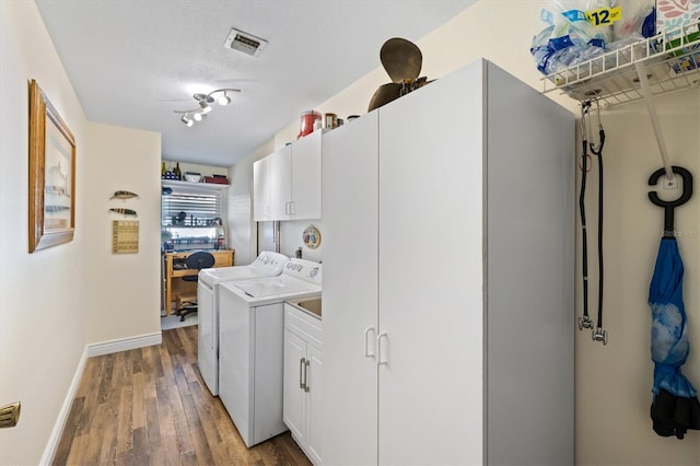 clothes washing area featuring washer and dryer, cabinets, wood-type flooring, and a textured ceiling