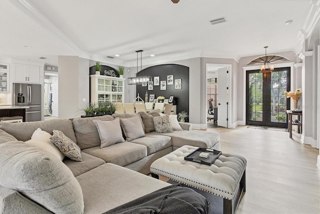 living room with french doors, light wood-type flooring, ornamental molding, and a chandelier