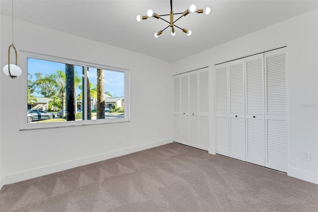 unfurnished bedroom with carpet, a textured ceiling, multiple closets, and a notable chandelier