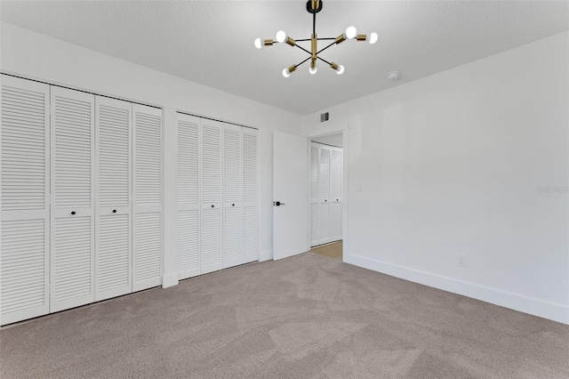 unfurnished bedroom with a textured ceiling, light carpet, a chandelier, and two closets