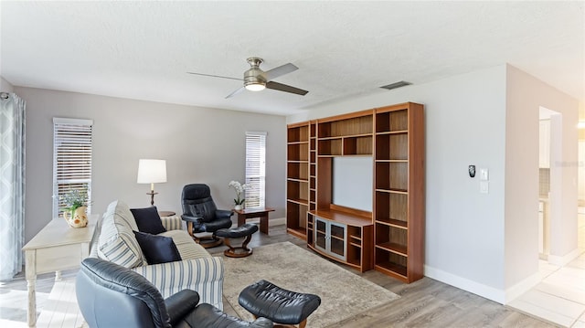 living area with a textured ceiling, light hardwood / wood-style floors, ceiling fan, and a healthy amount of sunlight