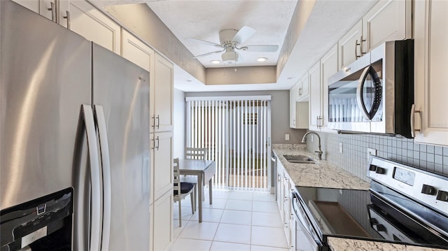 kitchen with light stone countertops, decorative backsplash, stainless steel appliances, sink, and white cabinetry