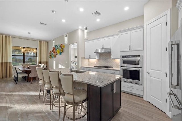 kitchen featuring a kitchen island with sink, sink, hanging light fixtures, white cabinetry, and stainless steel appliances