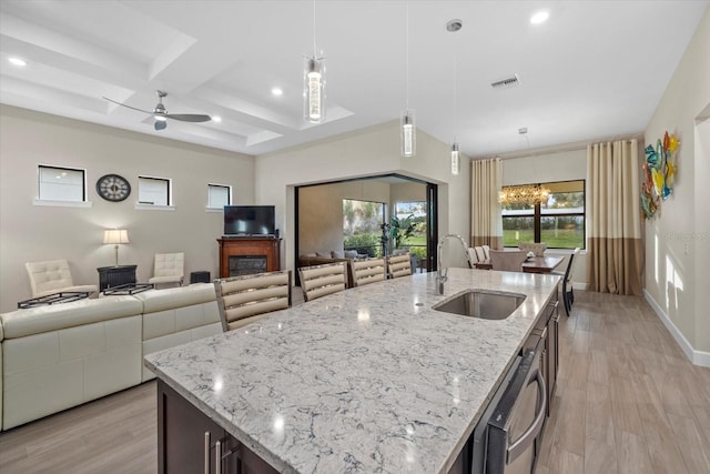 kitchen featuring a center island with sink, sink, hanging light fixtures, light hardwood / wood-style flooring, and light stone counters