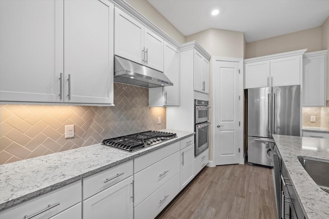 kitchen with white cabinetry, light stone countertops, backsplash, appliances with stainless steel finishes, and light wood-type flooring