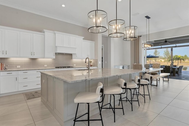 kitchen featuring ceiling fan with notable chandelier, white cabinetry, a kitchen island with sink, and sink