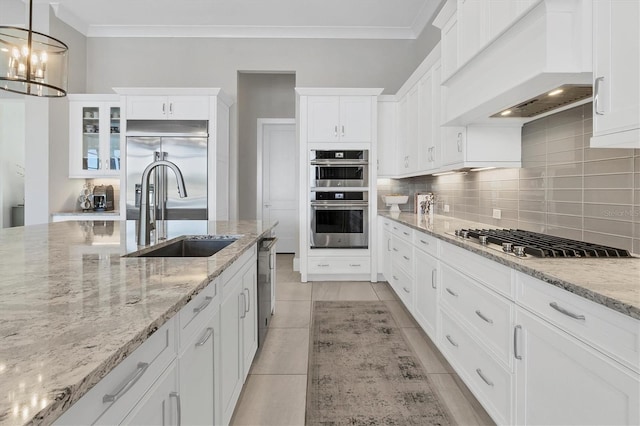 kitchen with pendant lighting, custom exhaust hood, sink, appliances with stainless steel finishes, and white cabinetry