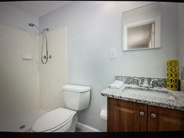 bathroom with vanity, toilet, and tiled shower