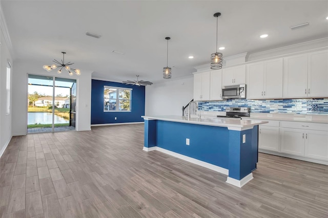 kitchen featuring appliances with stainless steel finishes, a center island with sink, white cabinetry, and hanging light fixtures