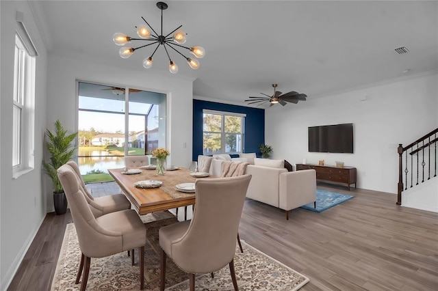 dining area with hardwood / wood-style flooring, ceiling fan with notable chandelier, a water view, and ornamental molding