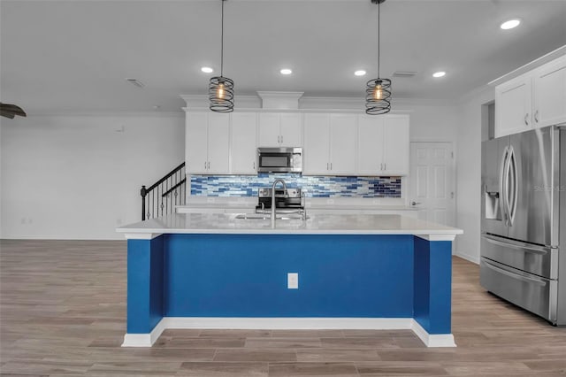 kitchen featuring stainless steel appliances, an island with sink, light hardwood / wood-style floors, decorative light fixtures, and white cabinets