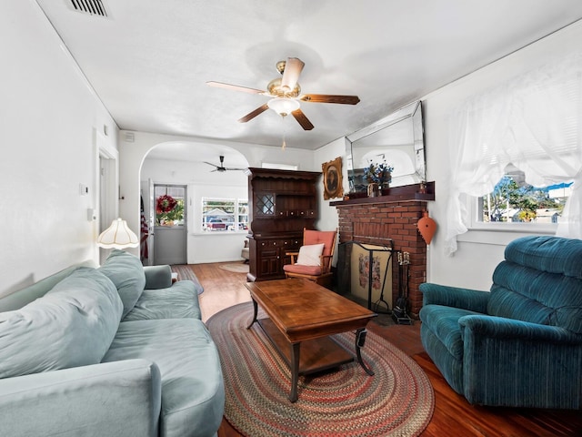 living room featuring ceiling fan, hardwood / wood-style floors, and a brick fireplace