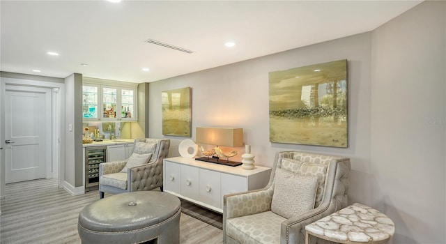 sitting room featuring indoor bar, light hardwood / wood-style floors, and wine cooler