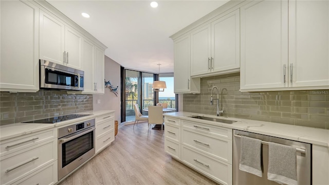 kitchen with pendant lighting, backsplash, sink, light hardwood / wood-style flooring, and appliances with stainless steel finishes