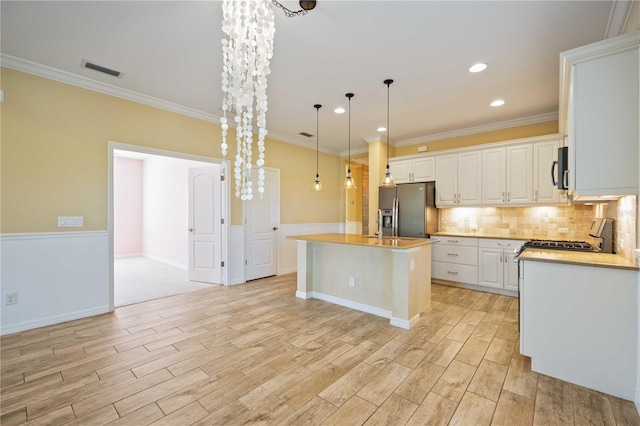 kitchen with a kitchen island with sink, white cabinets, crown molding, appliances with stainless steel finishes, and decorative light fixtures