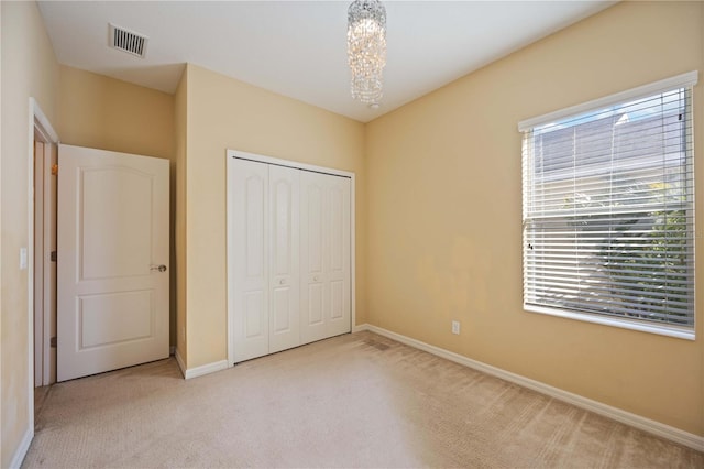 unfurnished bedroom featuring light carpet, an inviting chandelier, and a closet