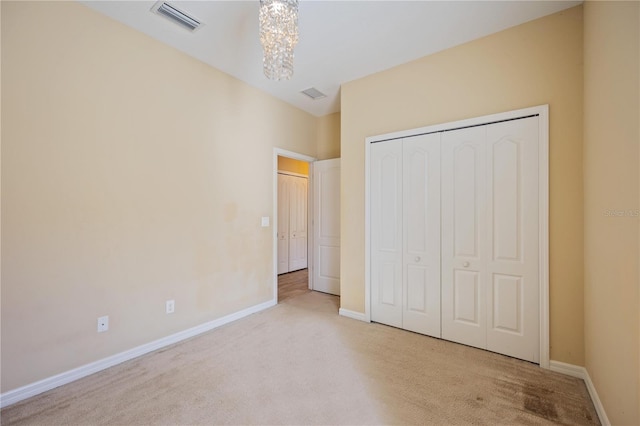 unfurnished bedroom with light colored carpet, a closet, and a notable chandelier