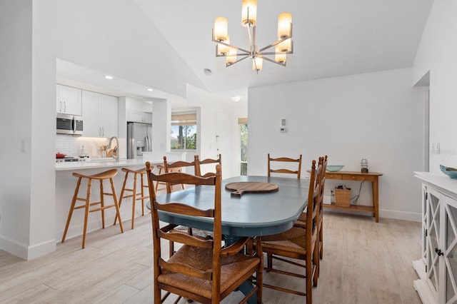 dining area featuring sink, high vaulted ceiling, a notable chandelier, and light wood-type flooring