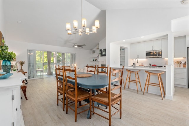 dining space with ceiling fan with notable chandelier, light hardwood / wood-style flooring, high vaulted ceiling, and sink