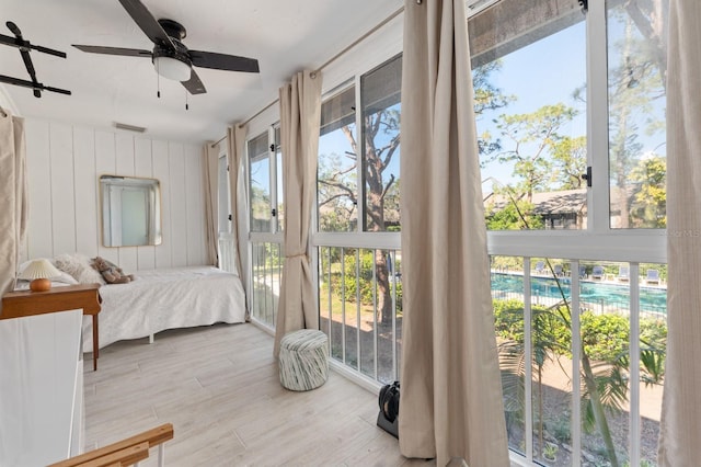 bedroom with ceiling fan, wood walls, and light wood-type flooring