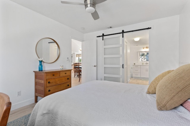 bedroom featuring ensuite bathroom, a barn door, light hardwood / wood-style floors, and ceiling fan