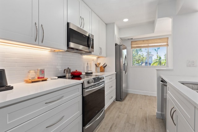 kitchen with white cabinets, decorative backsplash, stainless steel appliances, and light hardwood / wood-style floors