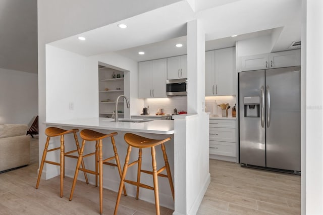 kitchen with appliances with stainless steel finishes, a kitchen breakfast bar, tasteful backsplash, sink, and white cabinetry